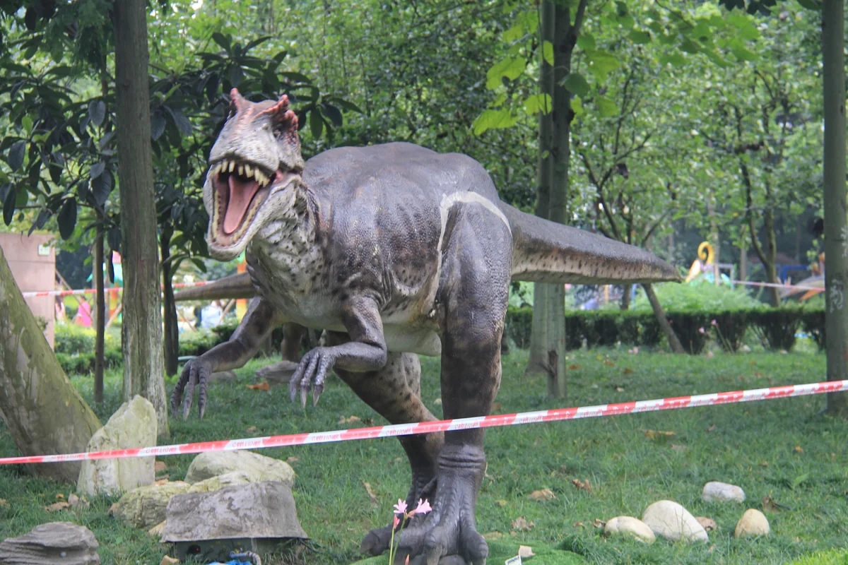 Allosaurus ride unit standing on grass in a park with the head raised