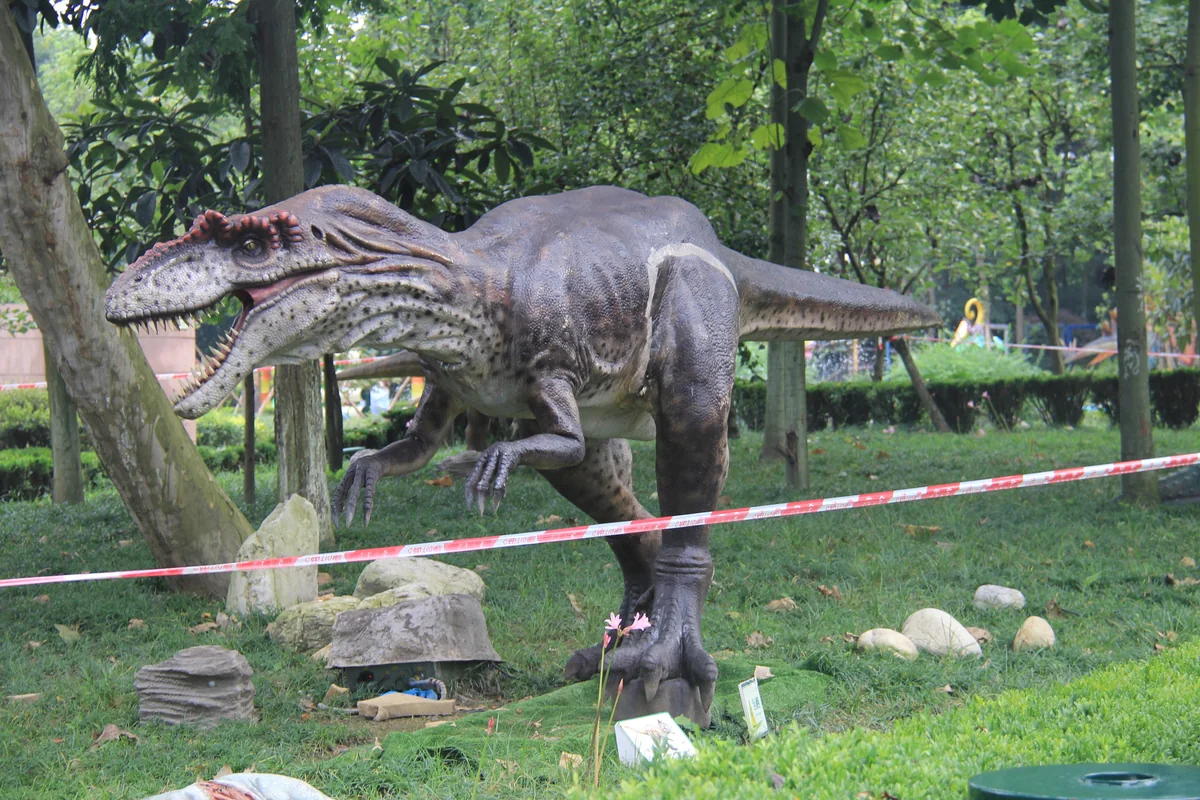 Allosaurus ride unit in a walking pose among trees in a park