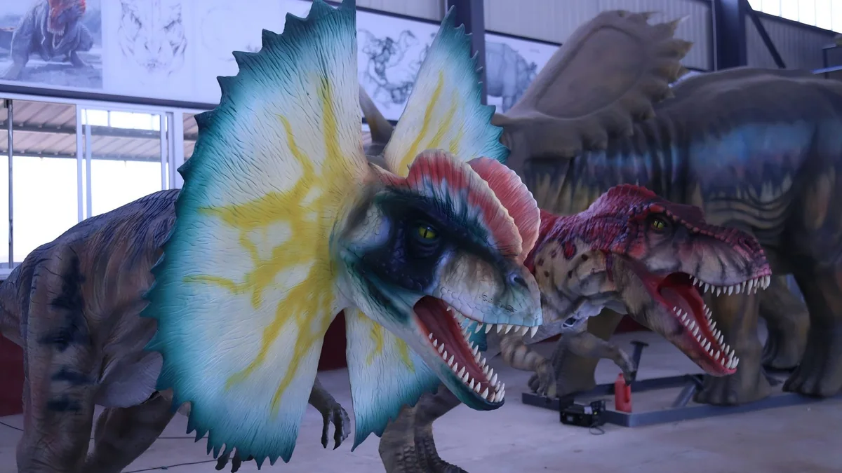 Close-up detail of animatronic Dilophosaurus with expanded neck frill and Spinosaurus showing lifelike eyes, teeth, and textured surface finish.