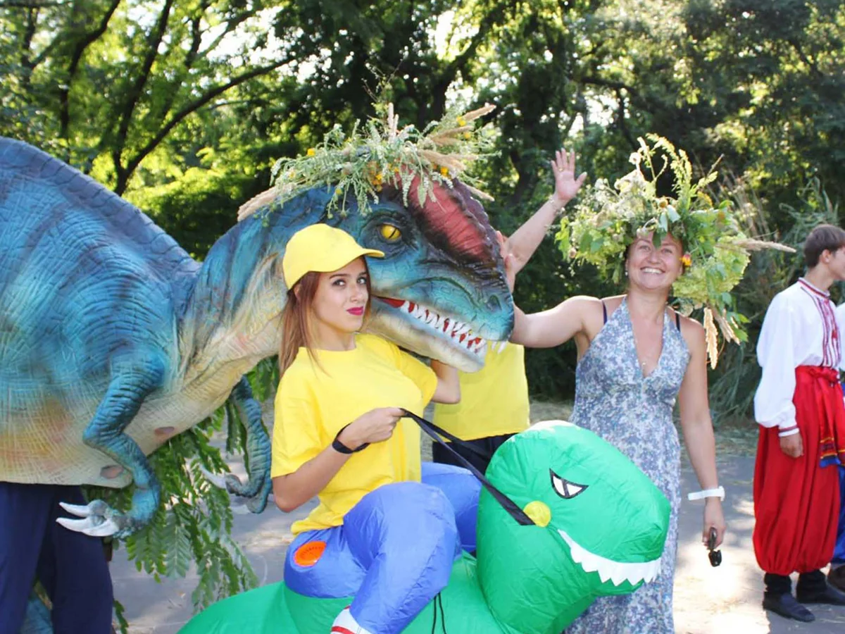 Performer in a walking dinosaur costume meeting visitors at an outdoor event