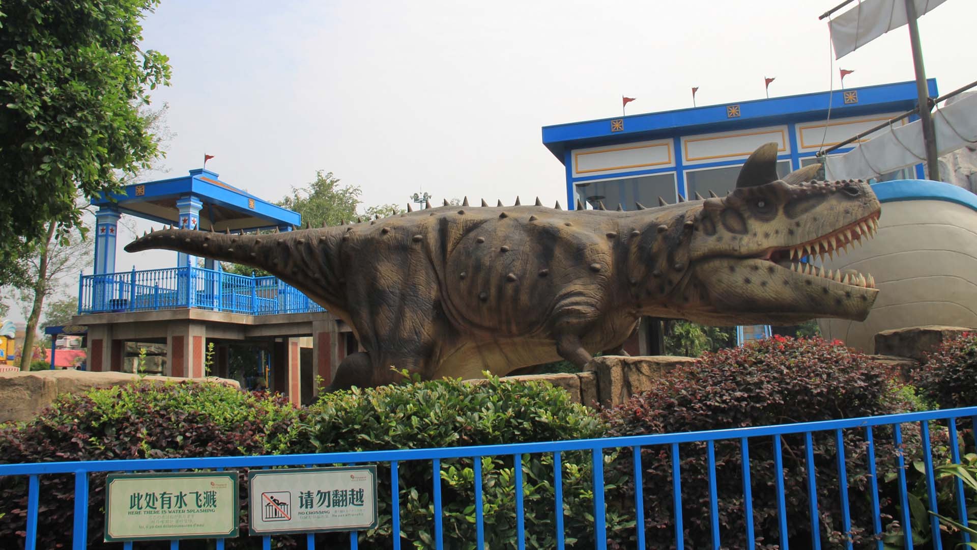 Life-size animatronic Carnotaurus with curved horns installed in a landscaped park with railings