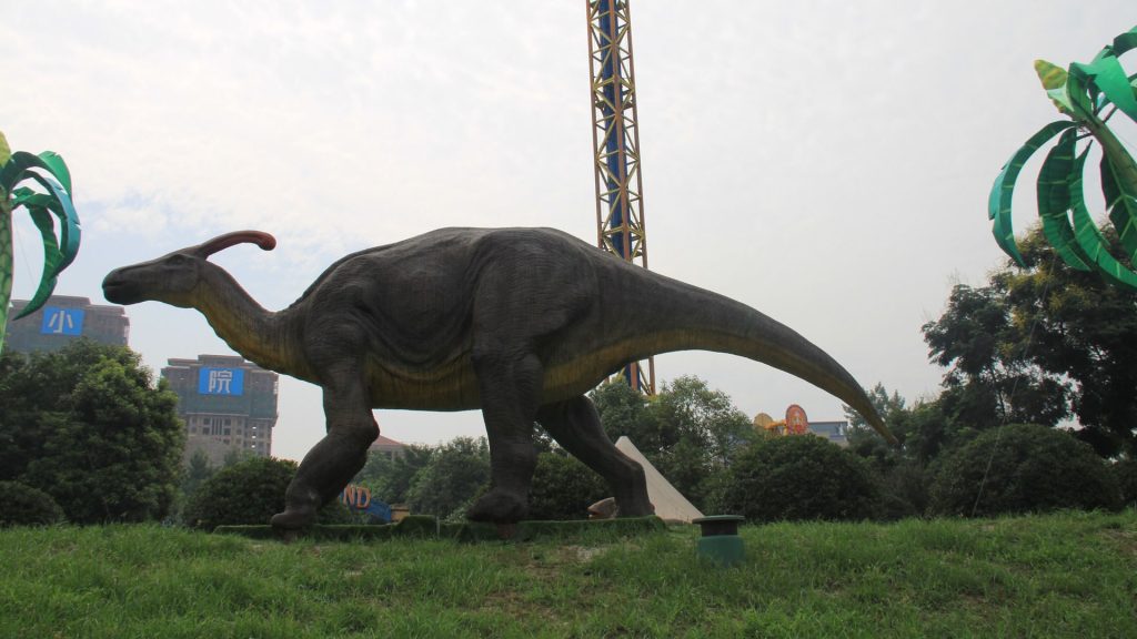 Animatronic Parasaurolophus model installed on a lawn in an open city park