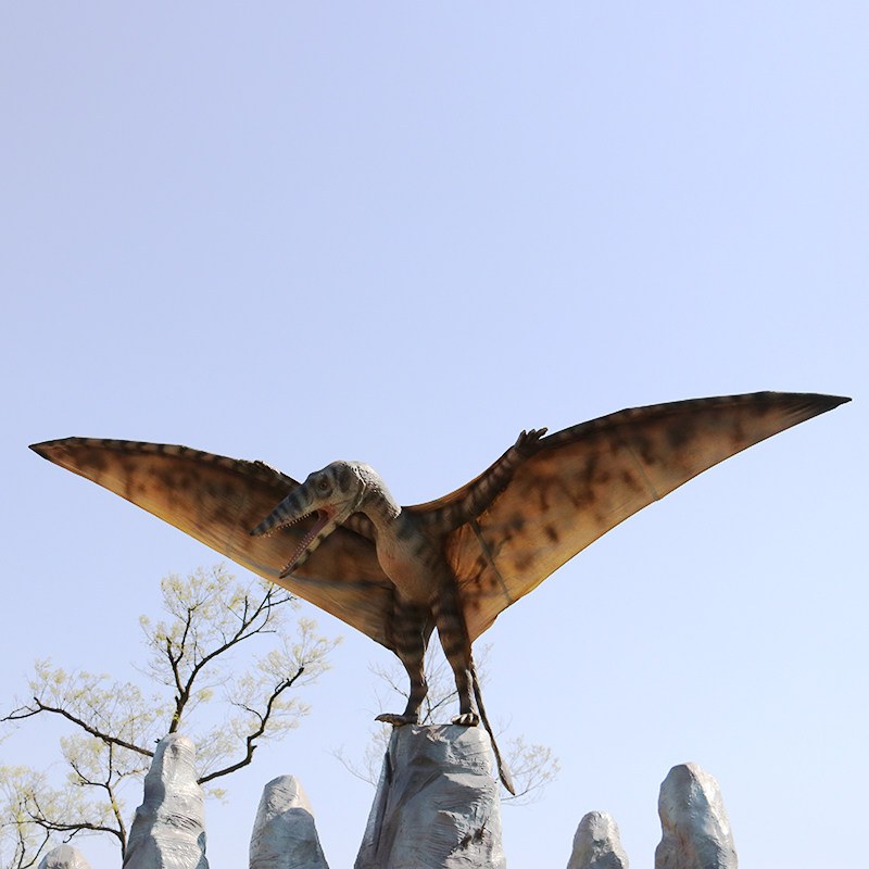 Life-size animatronic pterosaur model with spread wings perched on a stone column
