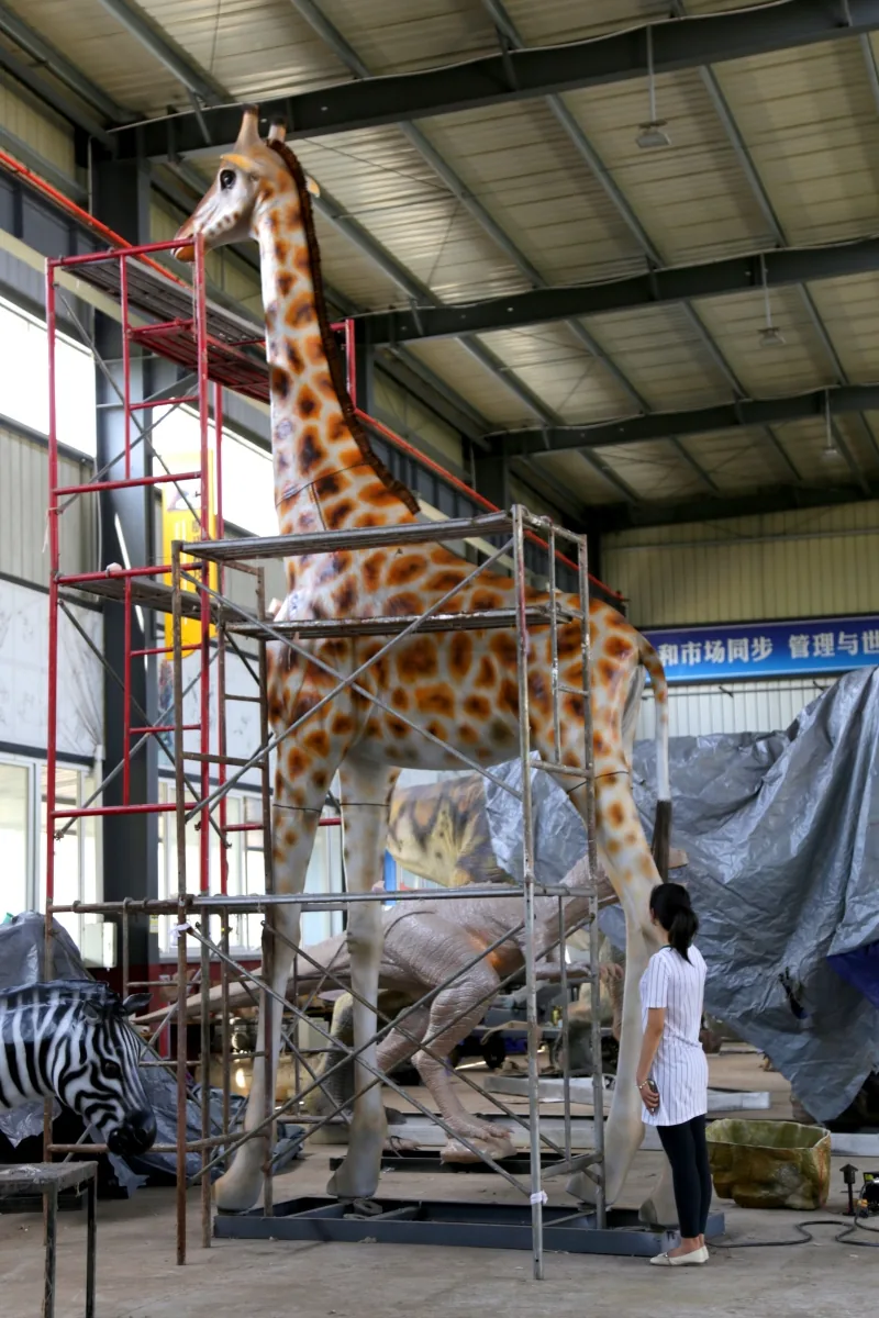 Life-size animatronic giraffe standing on a workshop platform next to a worker for scale