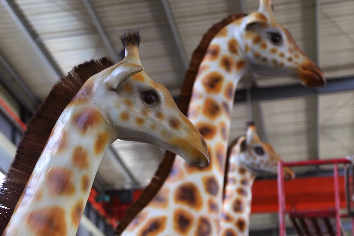 Row of animatronic giraffe heads in a workshop showing hand-painted coat patterns and ossicones