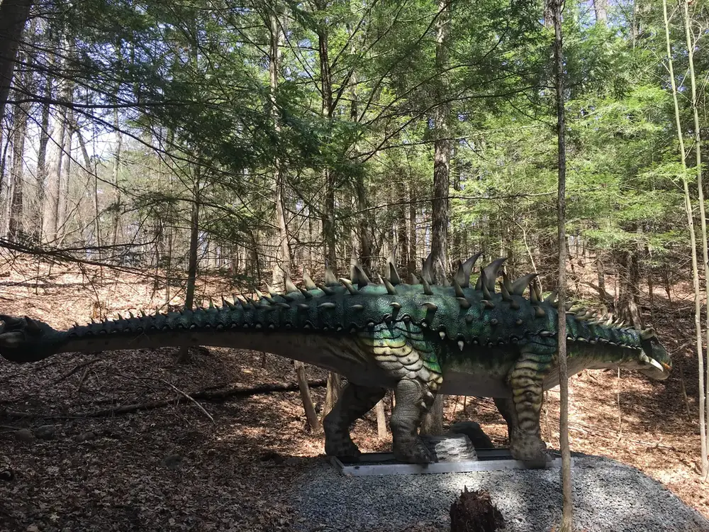 Life-size animatronic stegosaurus among trees at Lake George