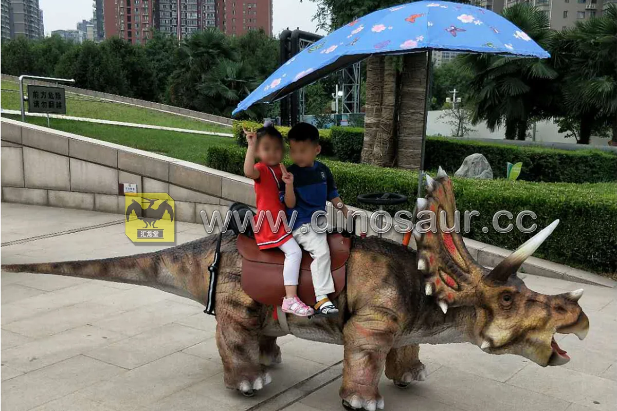 Animatronic dinosaur ride-on unit with a rider, shown outdoors on a park path