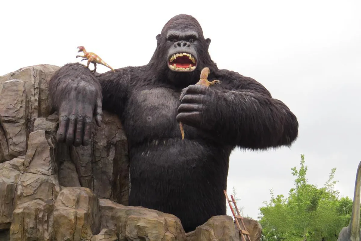 Large animatronic silverback gorilla seated on a rock formation in an outdoor park